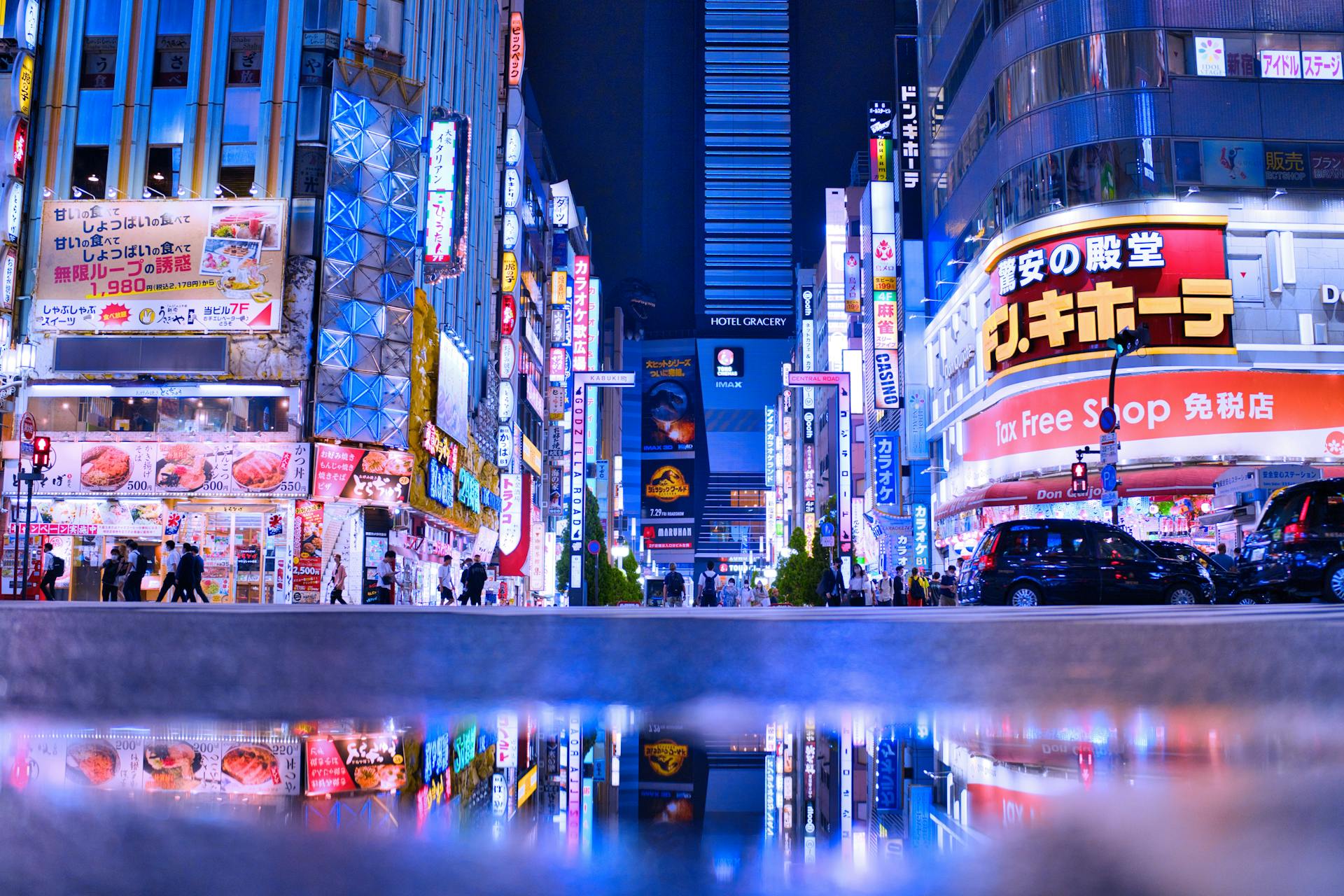 Shinjuku at night — neon signs reflected in rain-soaked streets, one of Tokyo's most iconic neighbourhoods for food, work cafés, and nightlife.